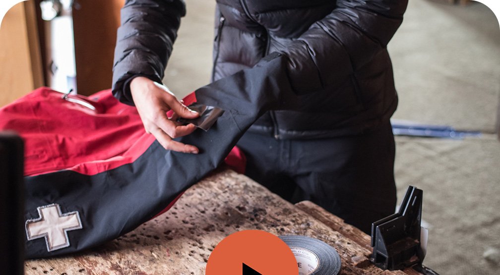 A ski patroller applies duct tape to a rip on the arm of her work jacket.