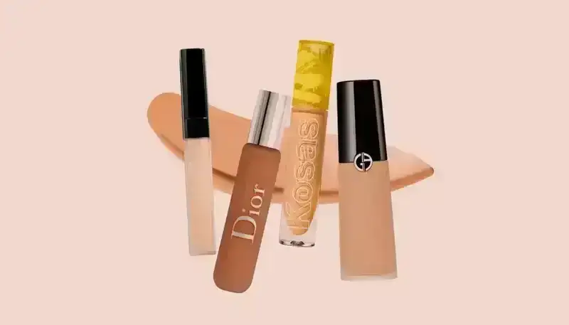 Undereye Concealers 2024: Tubes of concealer makeup from Nars, Dior, Kosas, and Armani on a beige-pink background.