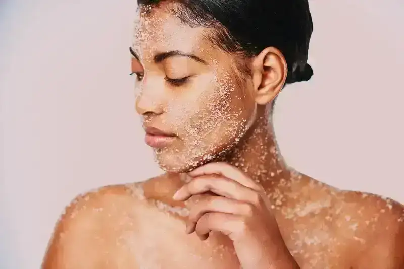 person with physical exfoliant on face and body