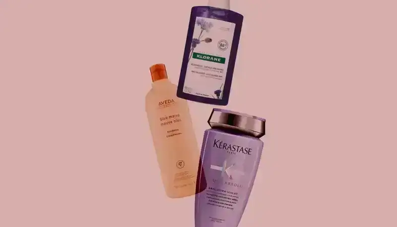 Best Shampoos for Gray Hair 2024: Bottles of shampoo from Kérastase, Aveda, and Klorane on a light pink background. 