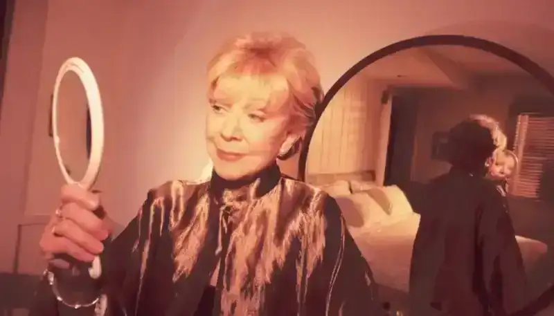 A photo of former Allure plastic surgery reporter Joan Kron looking in a mirror, with a mirror behind her and the reflection of a bed