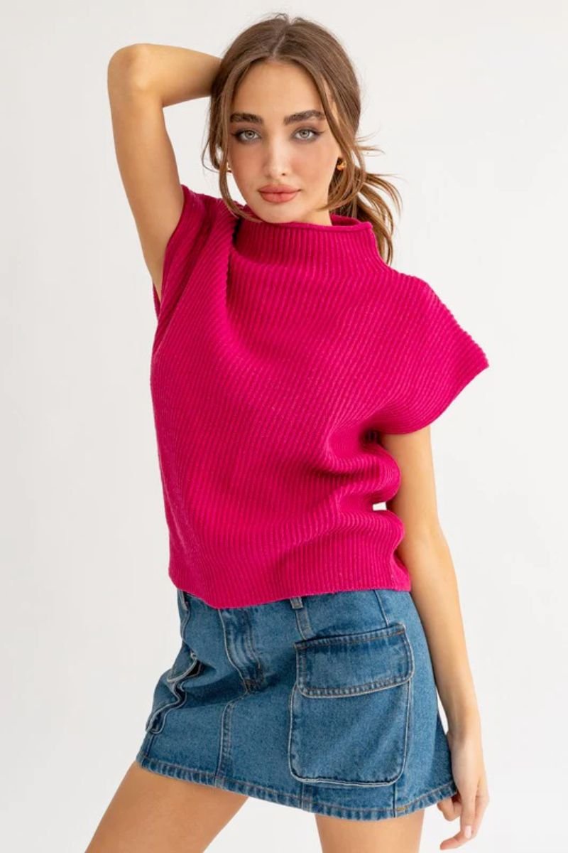 Turtle Neck Power Shoulder Sweater Vest. The model is wearing a fuchsia sweater best with short sleeves and a blue jean skirt.