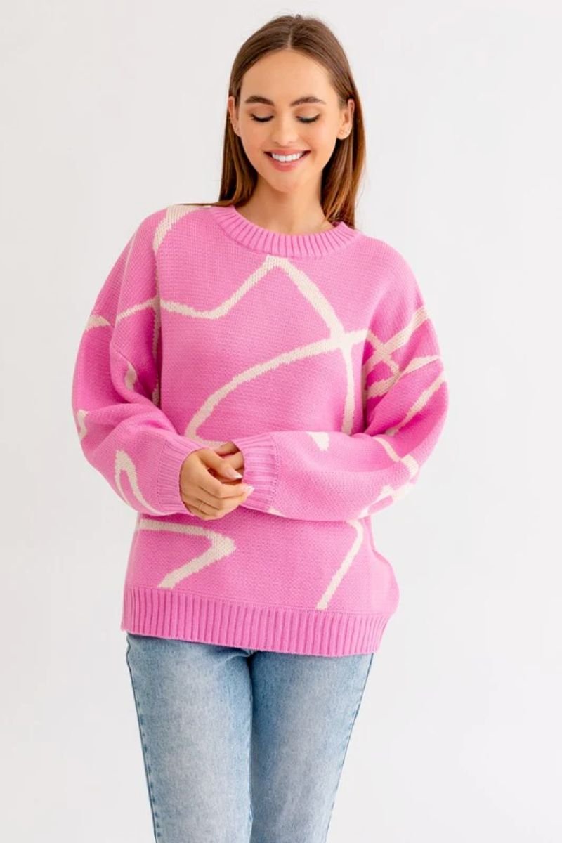 Abstract Pattern Oversized Sweater Top. The model is wearing a pink sweater with cream lines through it and blue jeans.