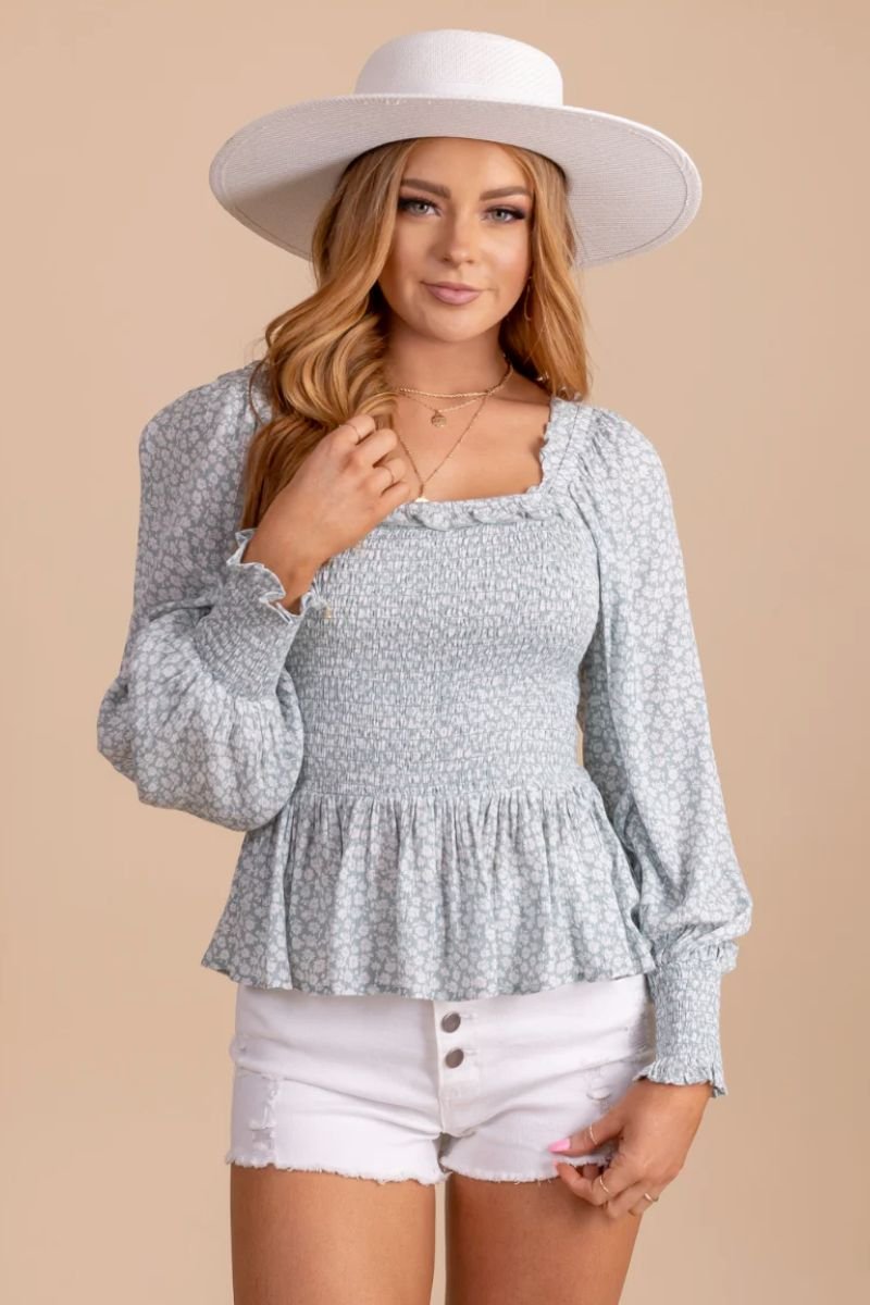 Desert Wildflower Smocked Long Sleeve Top. The model is wearing a blue floral shirt with a white hat and white short shorts.