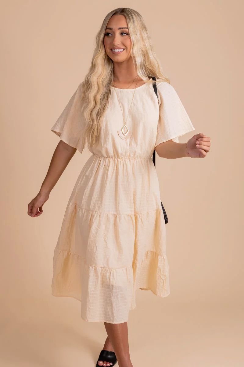 Chance to Shine Knee-Length Dress. The model is wearing an off white dress with multiple tiers and black shoes.