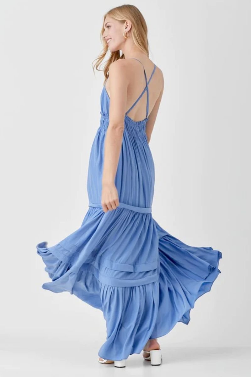 Shirred Ruffle Folded Detail Maxi Dress. The model is spinning in a blue dress with multiple tiers and crossed back straps. The model is also wearing white heels.