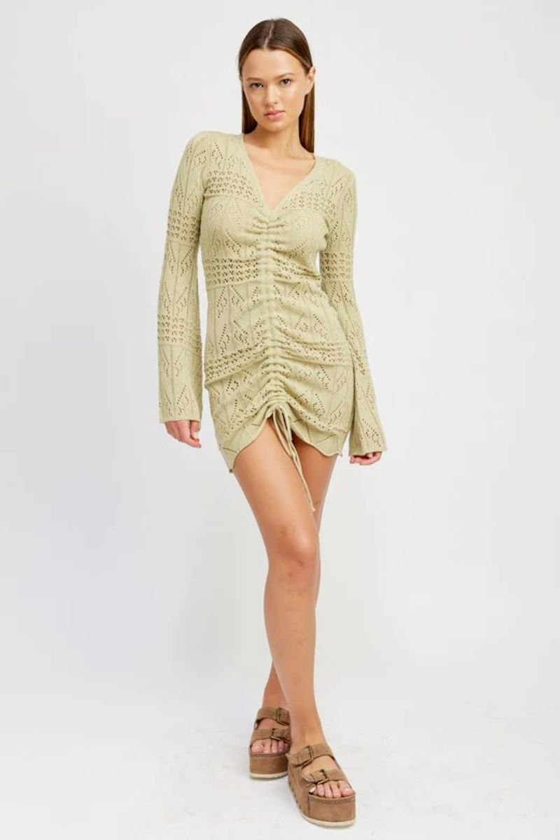 Ruched Crochet Mini Dress. The model is wearing a crochet dress that is ruched at the front with a tie that goes all the way down. The model is also wearing platform sandals.