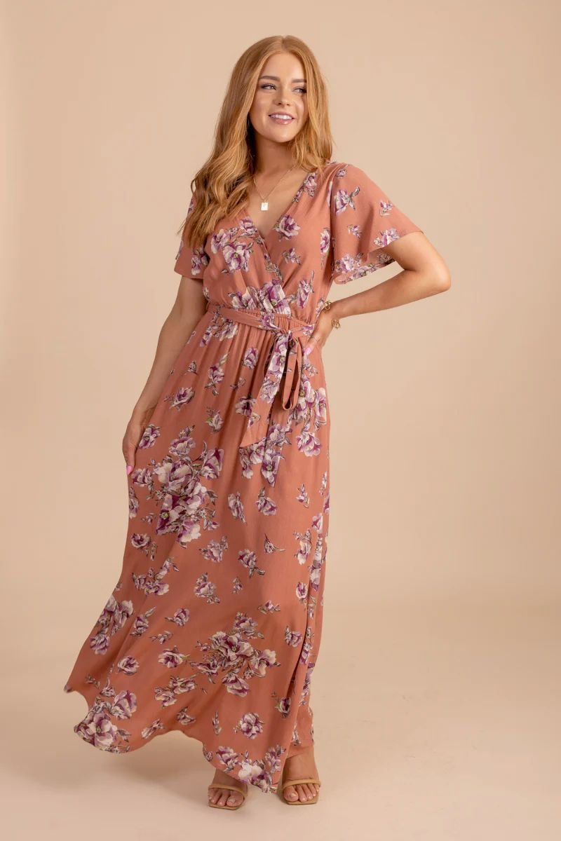 Bloomed Happiness Floral Maxi Dress. The model is wearing a wrap dress in a pink orange color with pink flowers on it.