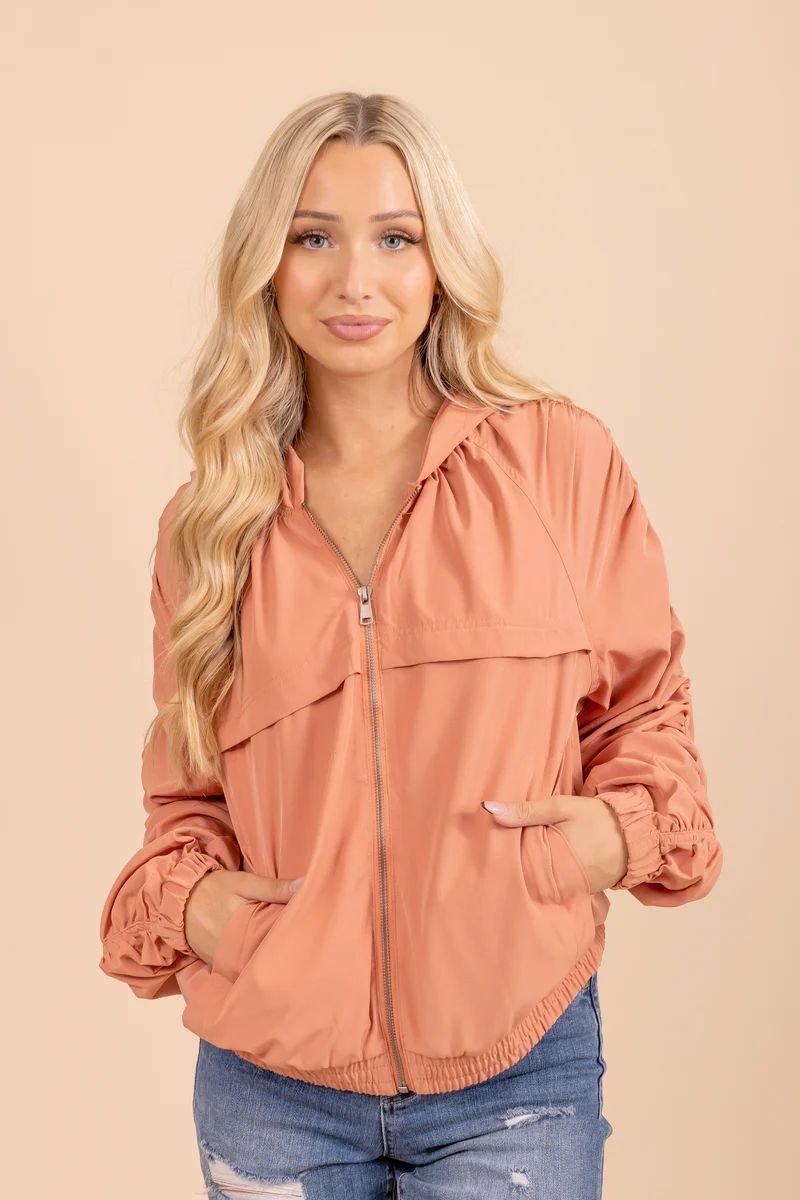 Zip Up Hooded Jacket With Ruched Sleeves. The model is wearing a rust jacket and has blonde hair.