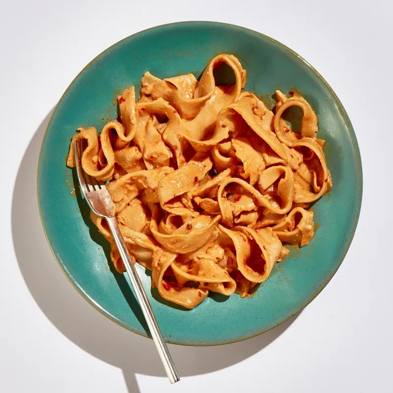 A blue bowl filled with saucy biang biang noodles, sitting on a white background.