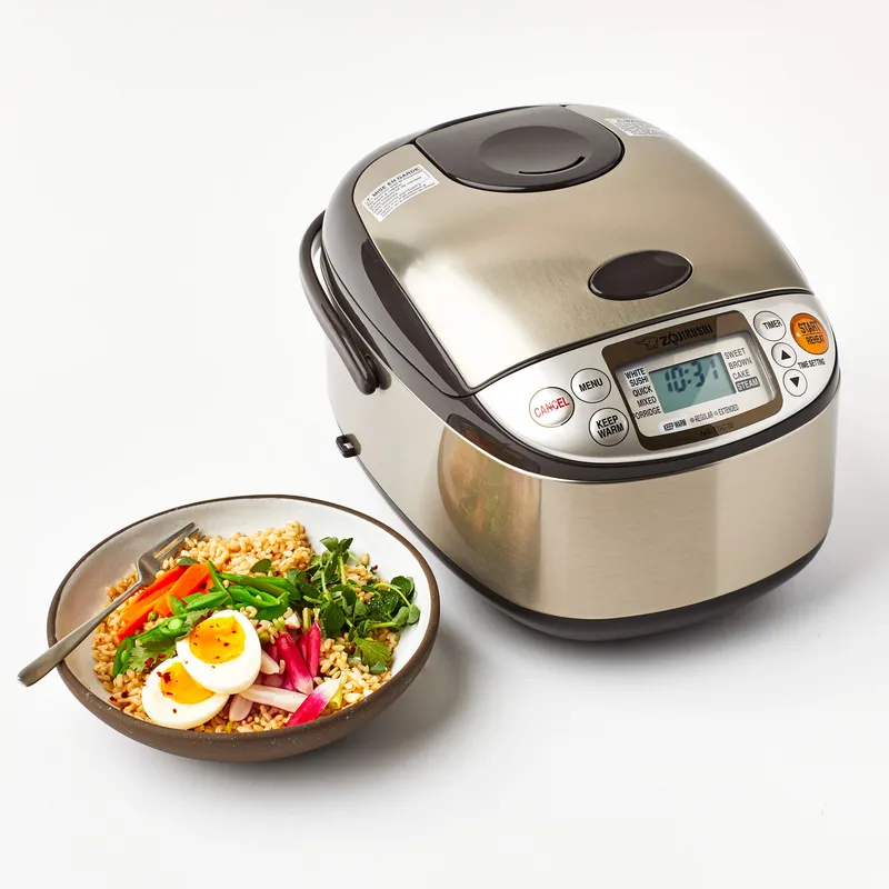 A Zojirushi rice cooker next to a rice bowl with vegetables and eggs