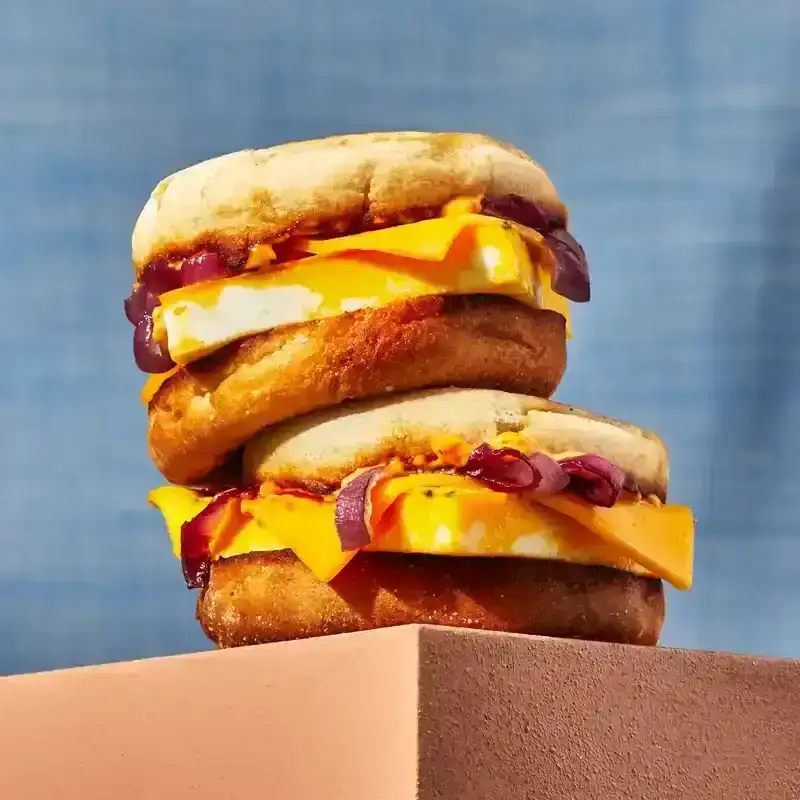 Two egg and cheese sandwiches on English muffins stacked on top of each other on top of a pink surface