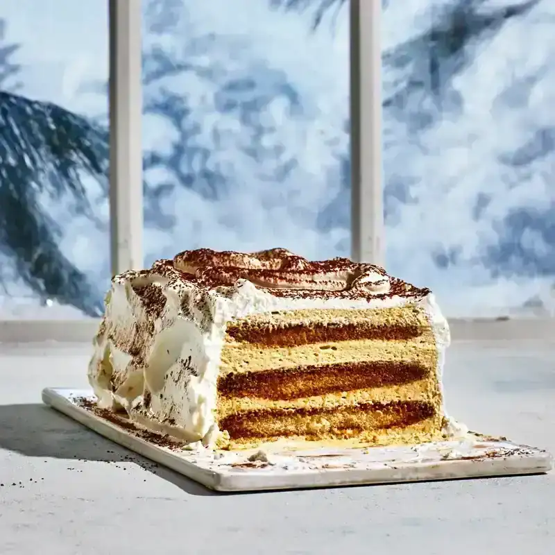 Shot of a rectangular sliced tiramisu ice box cake in front of a wintery window scene. 