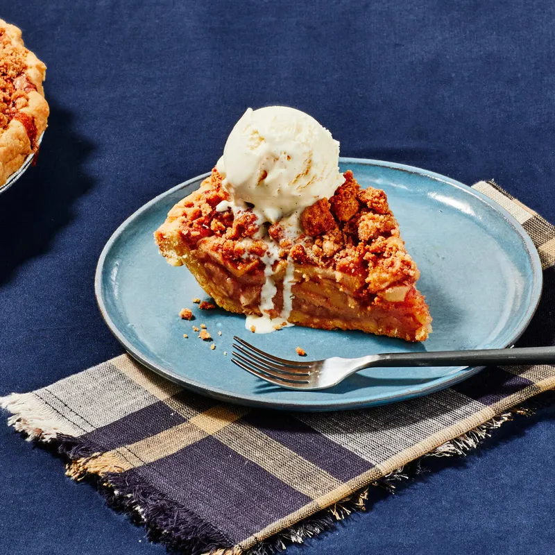 A slice of apple crumb pie on a plate, topped with a scoop of drippy vanilla ice cream.