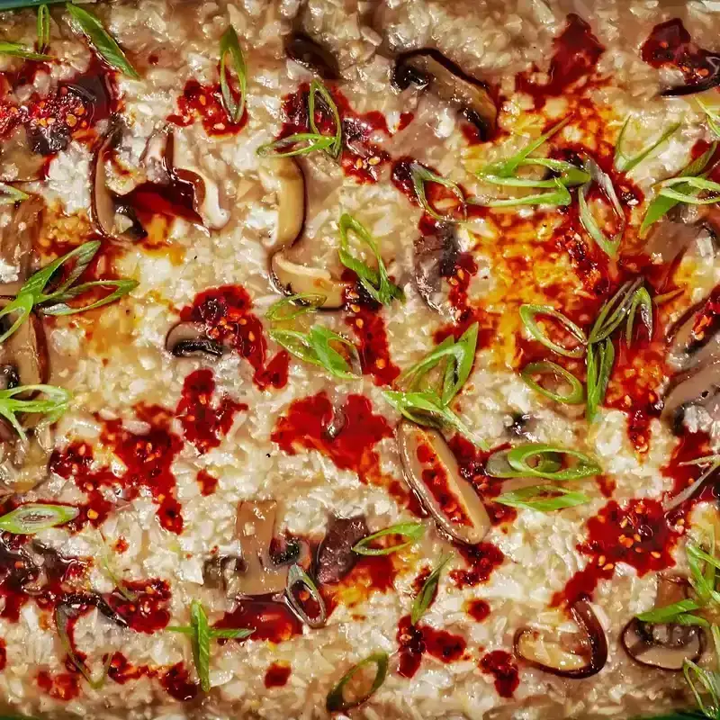 Baked Mushroom Rice Porridge in a green baking dish with chilli oil to the top right.