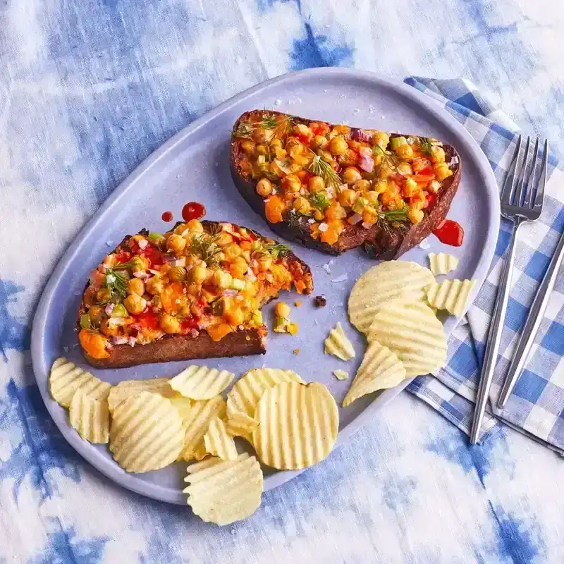 Cheesy chickpea salad toast, partially sliced into, with ridged potato chips on the side