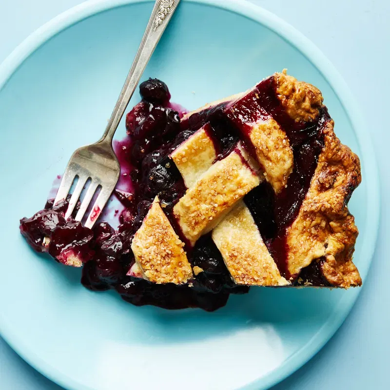 Overhead shot of a slice of lattice-topped blueberry pie on a plate with a bite removed and a fork resting on the side.