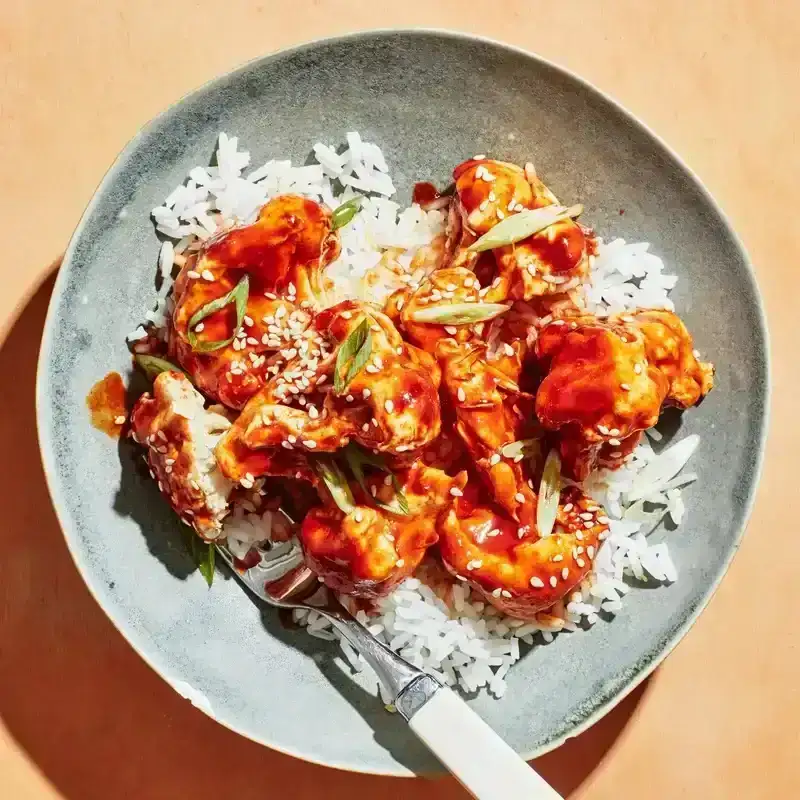 A plate of rice topped with a spicy red sauce coated cauliflower 