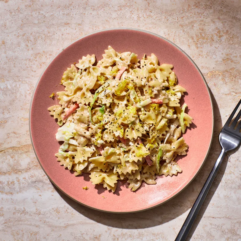 Creamy Sesame Pasta Slaw on a pink plate placed on stone.