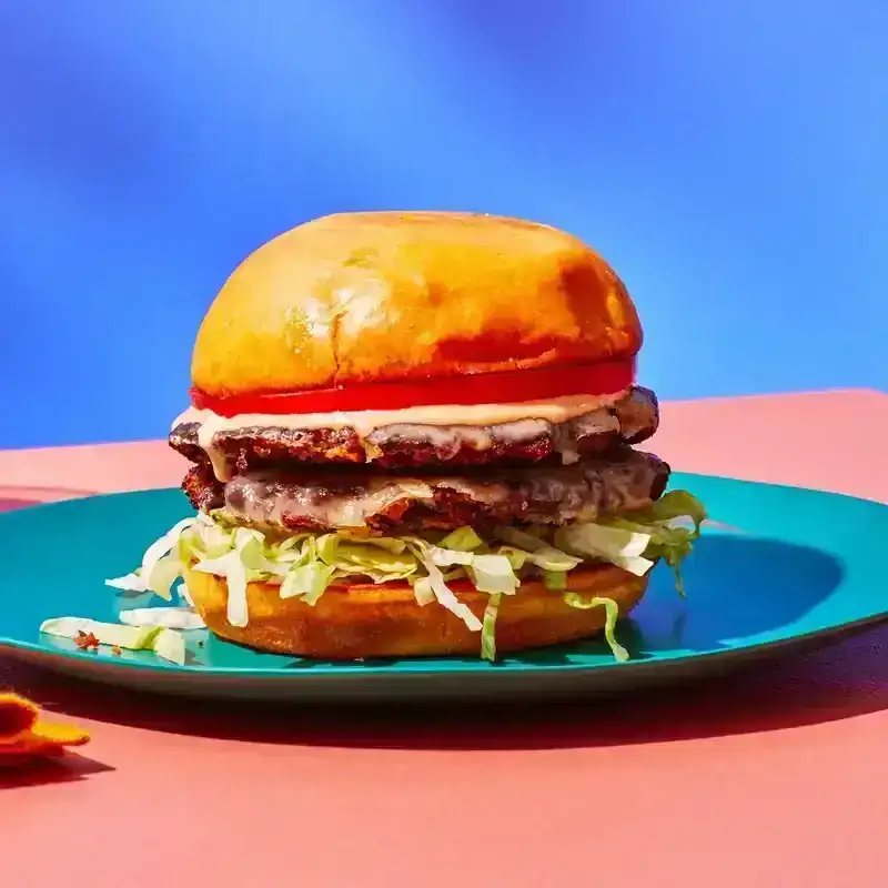 Side view of a black bean burger with two thin patties layered with shredded lettuce, tomato, and special sauce on a plate with a colorful background.