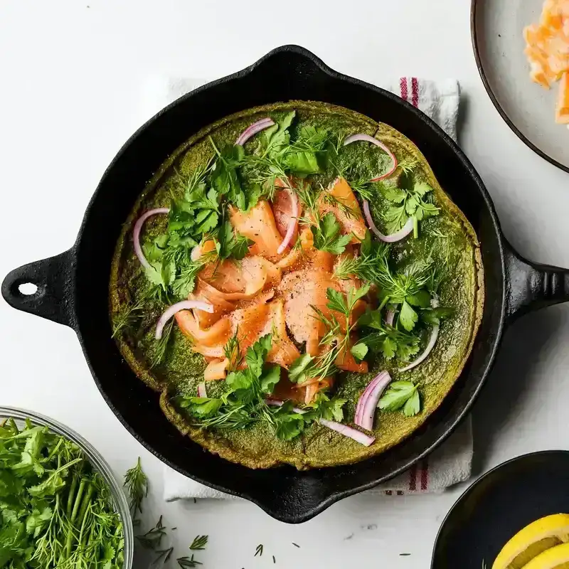 Green dutch baby with smoked salmon and herbs in a cast iron skillet