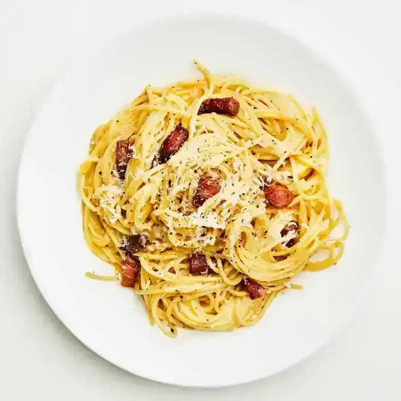 A plate of spaghetti carbonara with bits of crispy guanciale and topped with shredded cheese and black pepper.