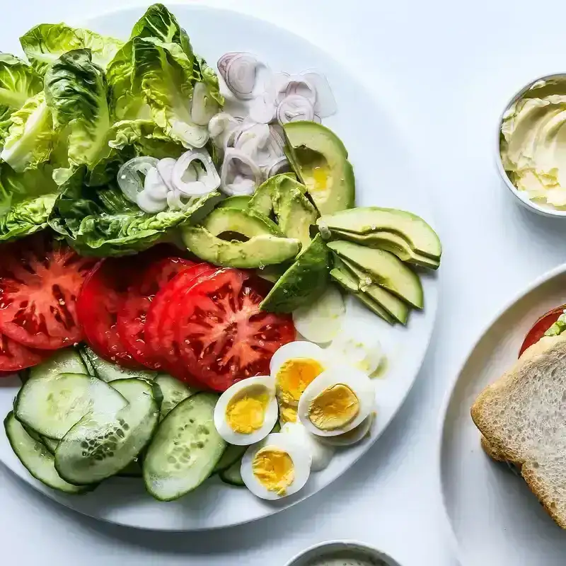 A platter with an easy lunch spread for making your own sandwiches with lettuce, sliced tomato, avocado, boiled eggs, shallots, and more.