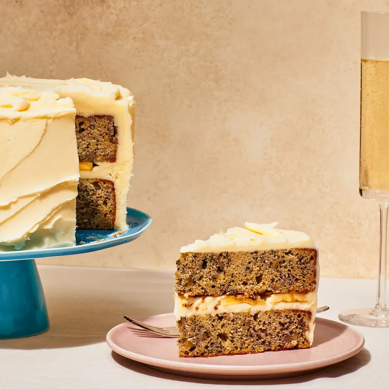 Double banana cake on a blue cake stand next to a cut slice with a glass of champagne. 