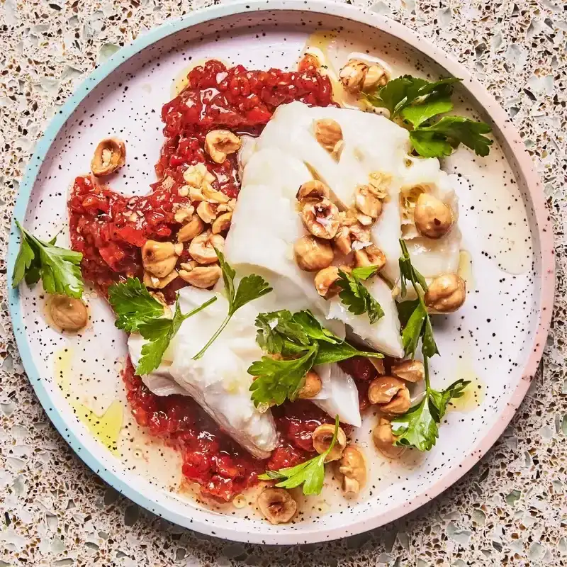 A flaky cod fillet set over a bright red sauce of chopped red peppers and topped with deeply toasted hazelnuts and parsley sprigs.