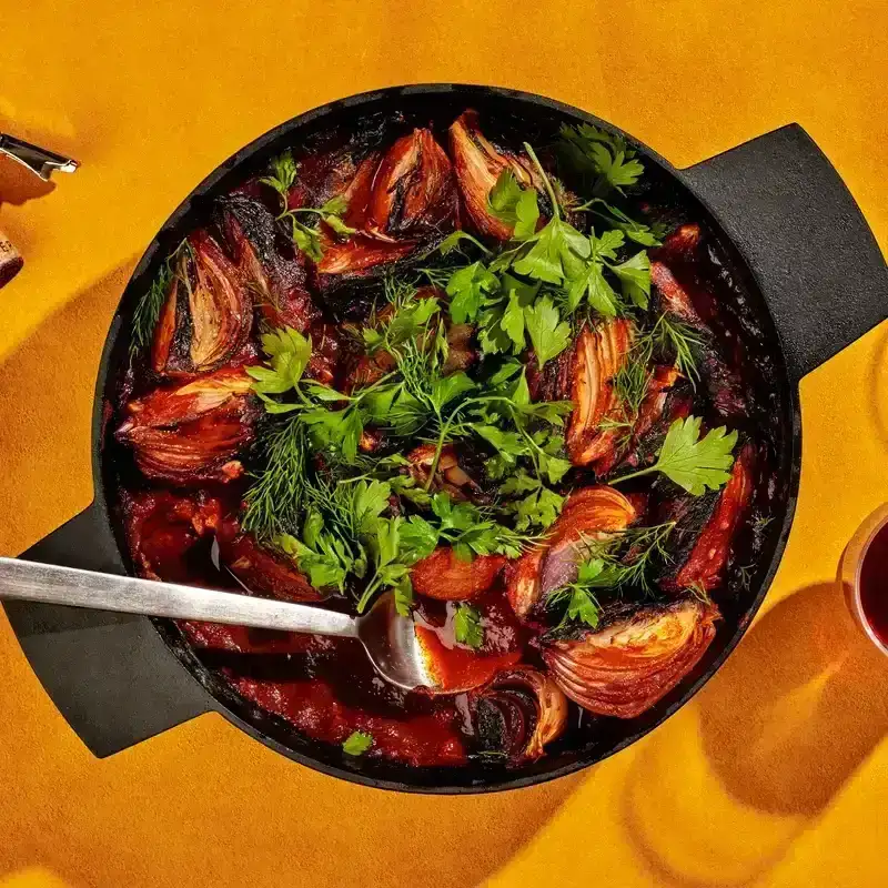 Tomato-Roasted Onions With Paprika in a dutch oven placed on a yellow surface