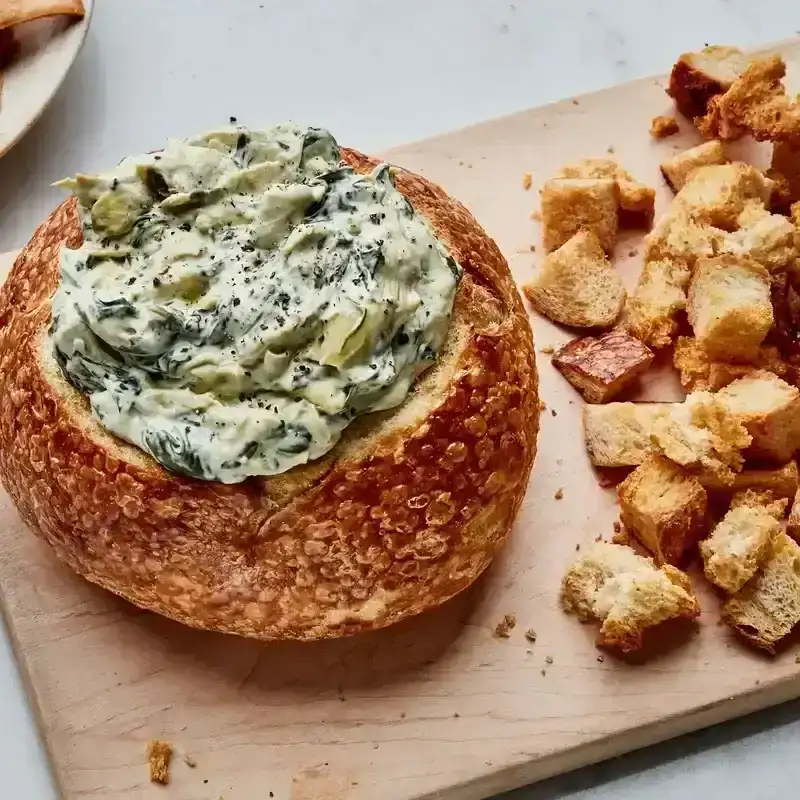 A creamy spinach and artichoke dip recipe filled to the brim of a crusty sourdough bread bowl.