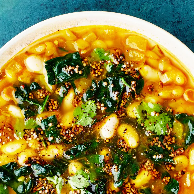 A plate of beans on a blue background with a side of cilantro and a glass of water