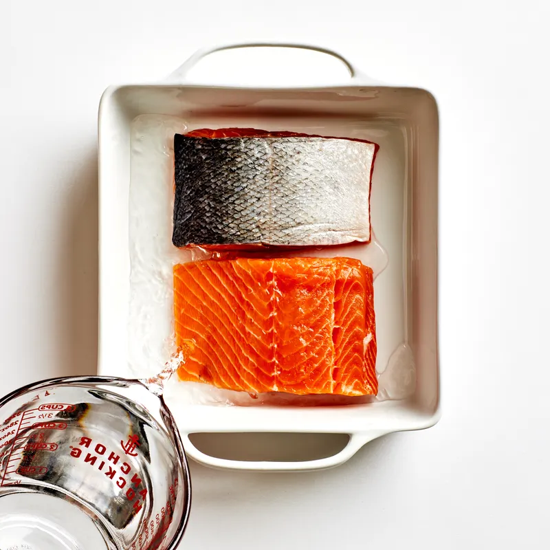 2 filet pieces of Salmon in a white bowl with water being poured on them