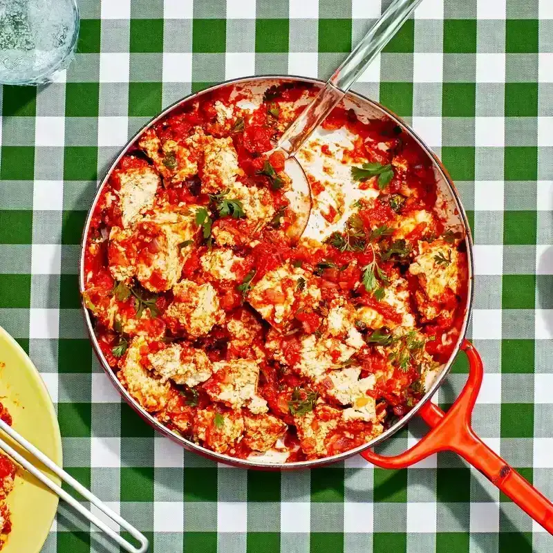 Pot of tofu with red sauce on green checkered tablecloth. 