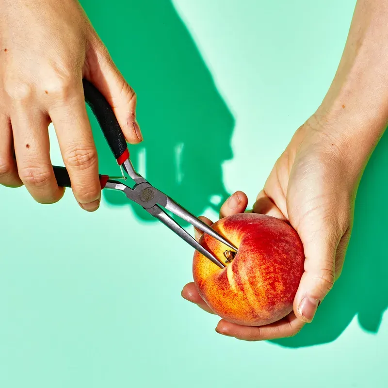 a set of hands pulling out a peach pit from a peach