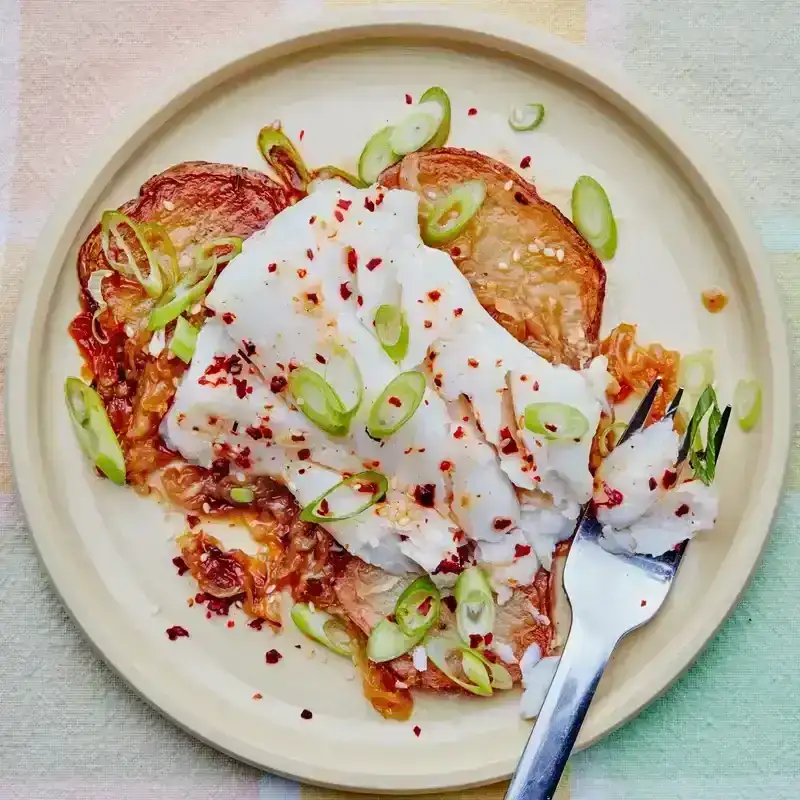 A cod fillet set on top of caramelized sliced potatoes, sprinkled with green onions and chile flakes.