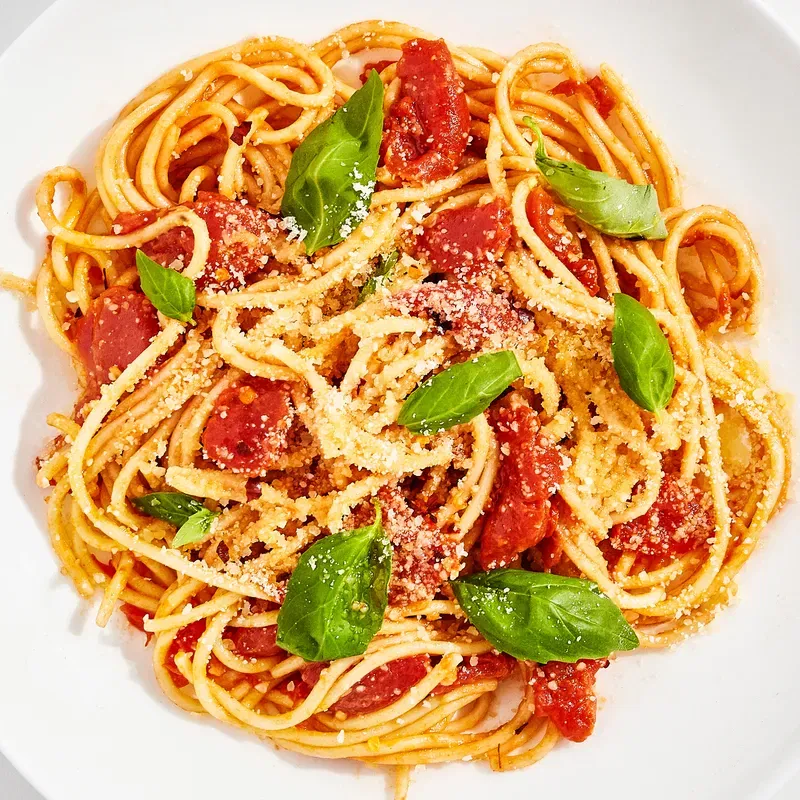 A serving bowl of pasta with pomodoro sauce topped with fresh basil leaves and Parmesan cheese.