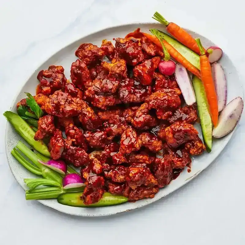 Harissa honey popcorn chicken on a platter with fresh veggies