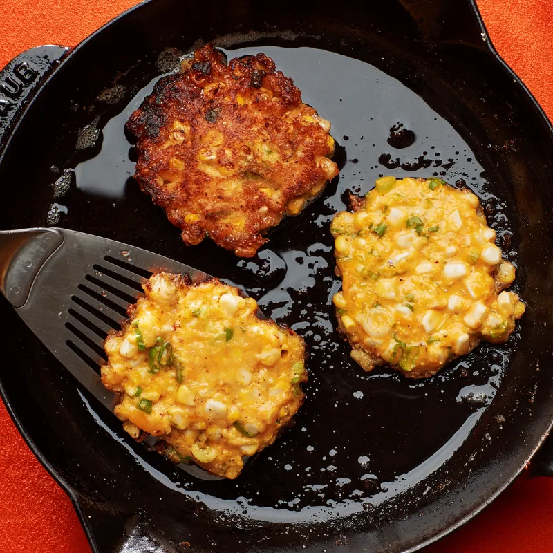 Corn fritters frying in a cast-iron skillet.