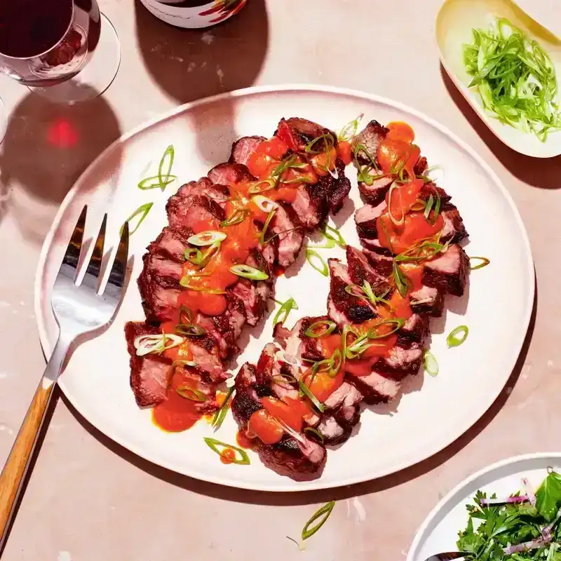 Plate with strips of steak with the butter sauce on top and a side salad on the corner