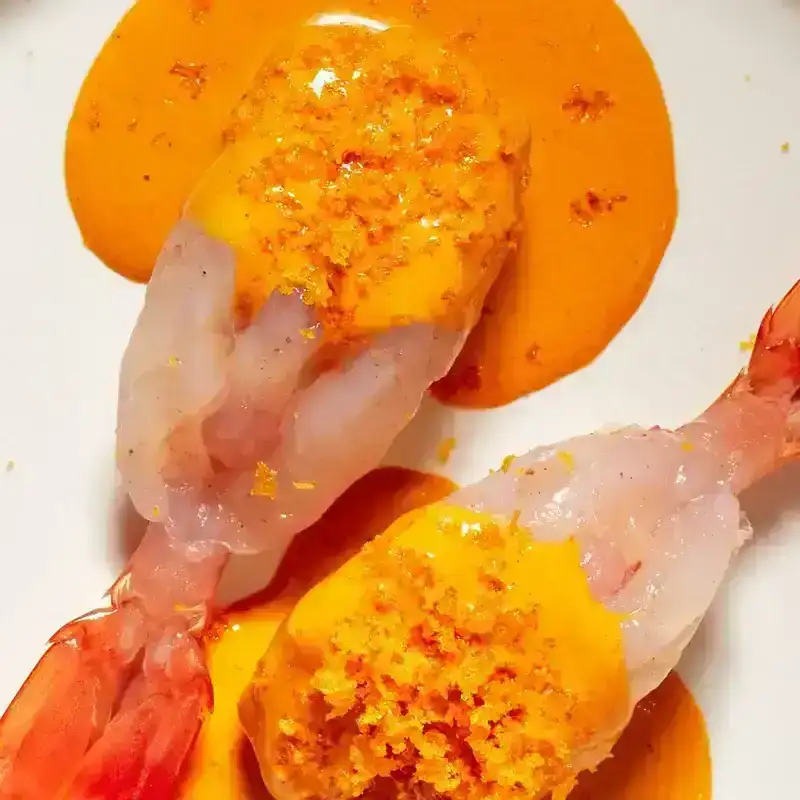 Two prawns with orange sauce on a white plate, set against a palm tree image.