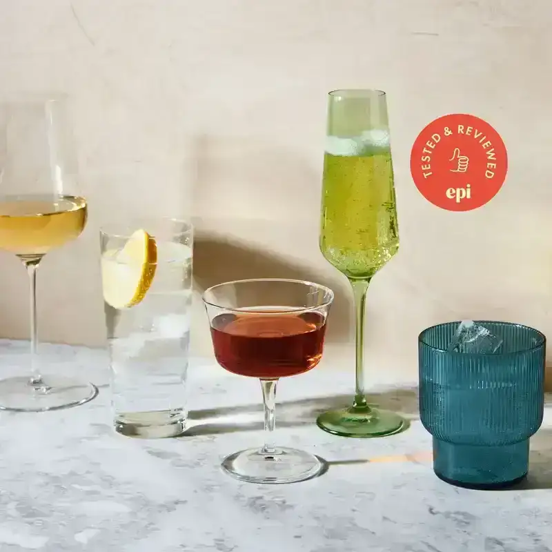 A wine glass, glass with seltzer, coupe, champagne glass, and plastic tumbler on a kitchen table.