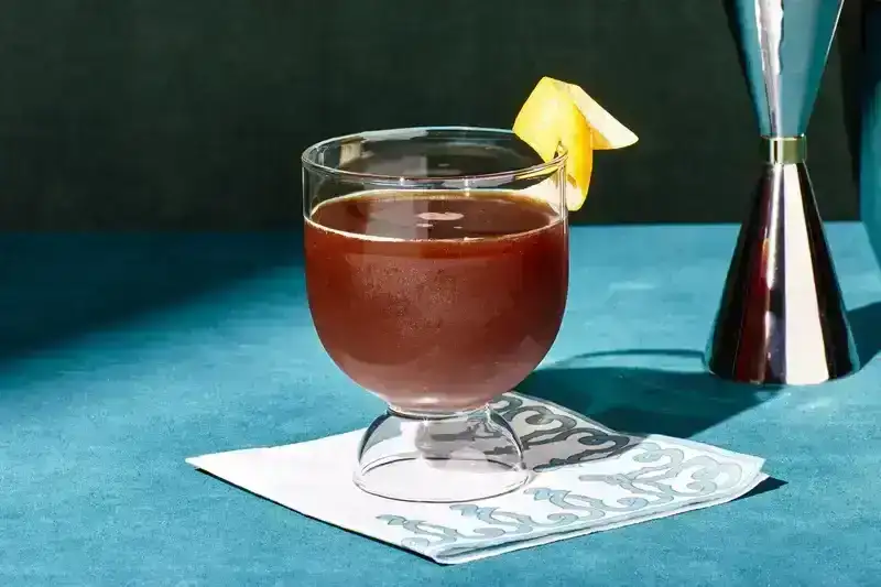 Brown drink with a lemon sitting on blue surface.