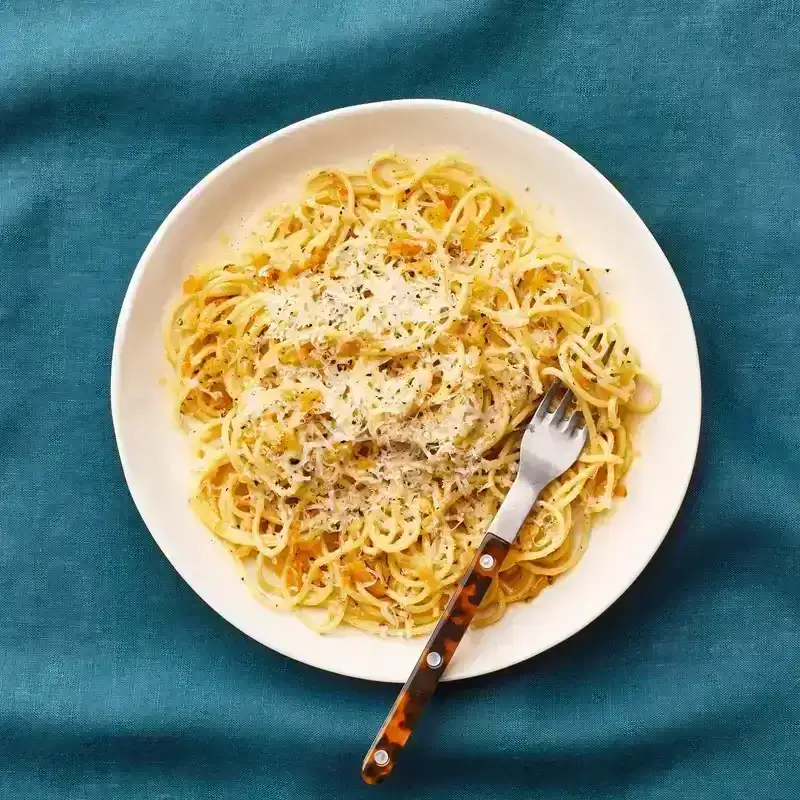 Plate of pasta with preserved lemon sauce topped with cheese and black pepper, with some pasta twirled around a fork.