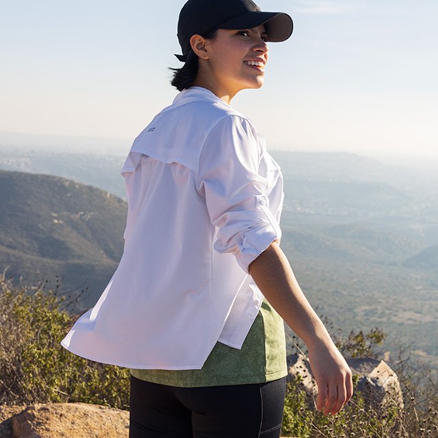 A woman stands at the top of a hill overlooking the scenery. 