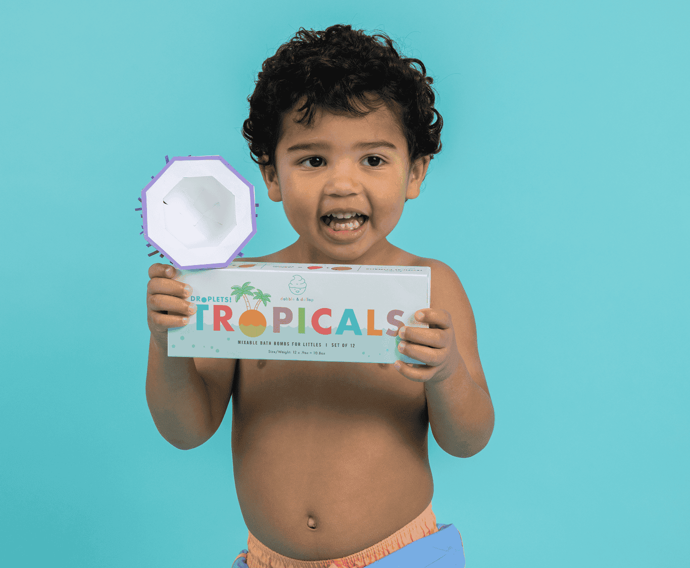 boy with curly hair holding box of tropical bath bombs and origami coconut half
