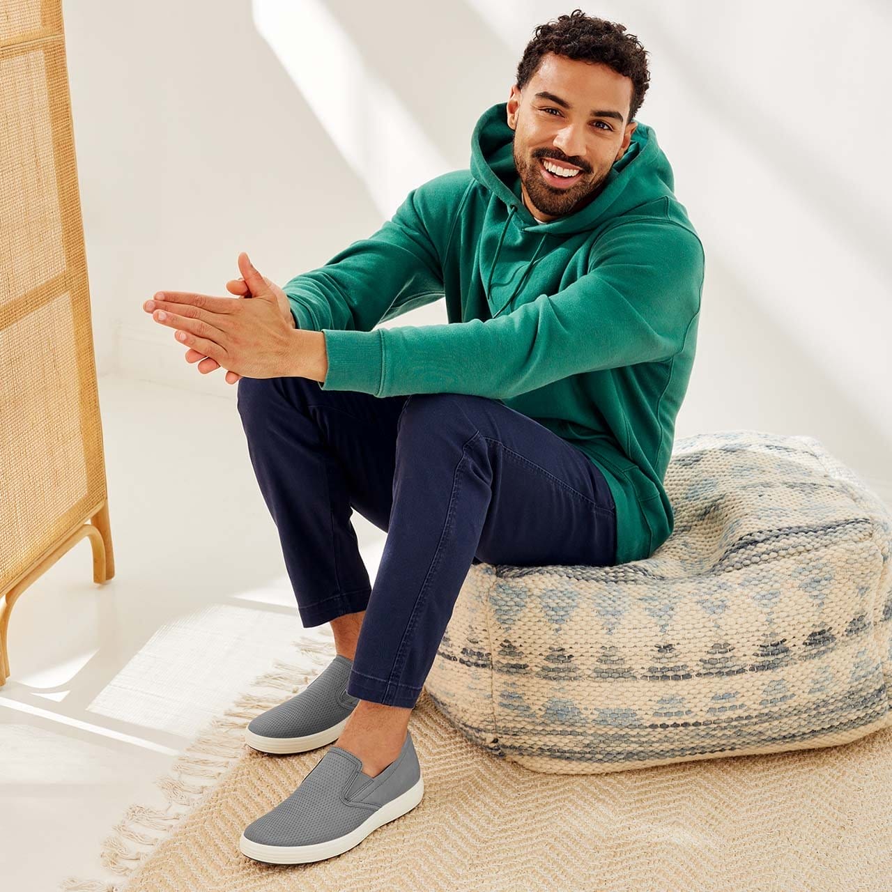 Man sitting on pouf wearing casual clothes and slip on sneakers