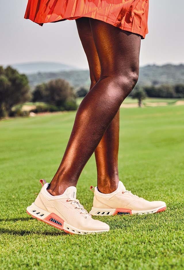 Woman on golf course wearing peach golf shoes
