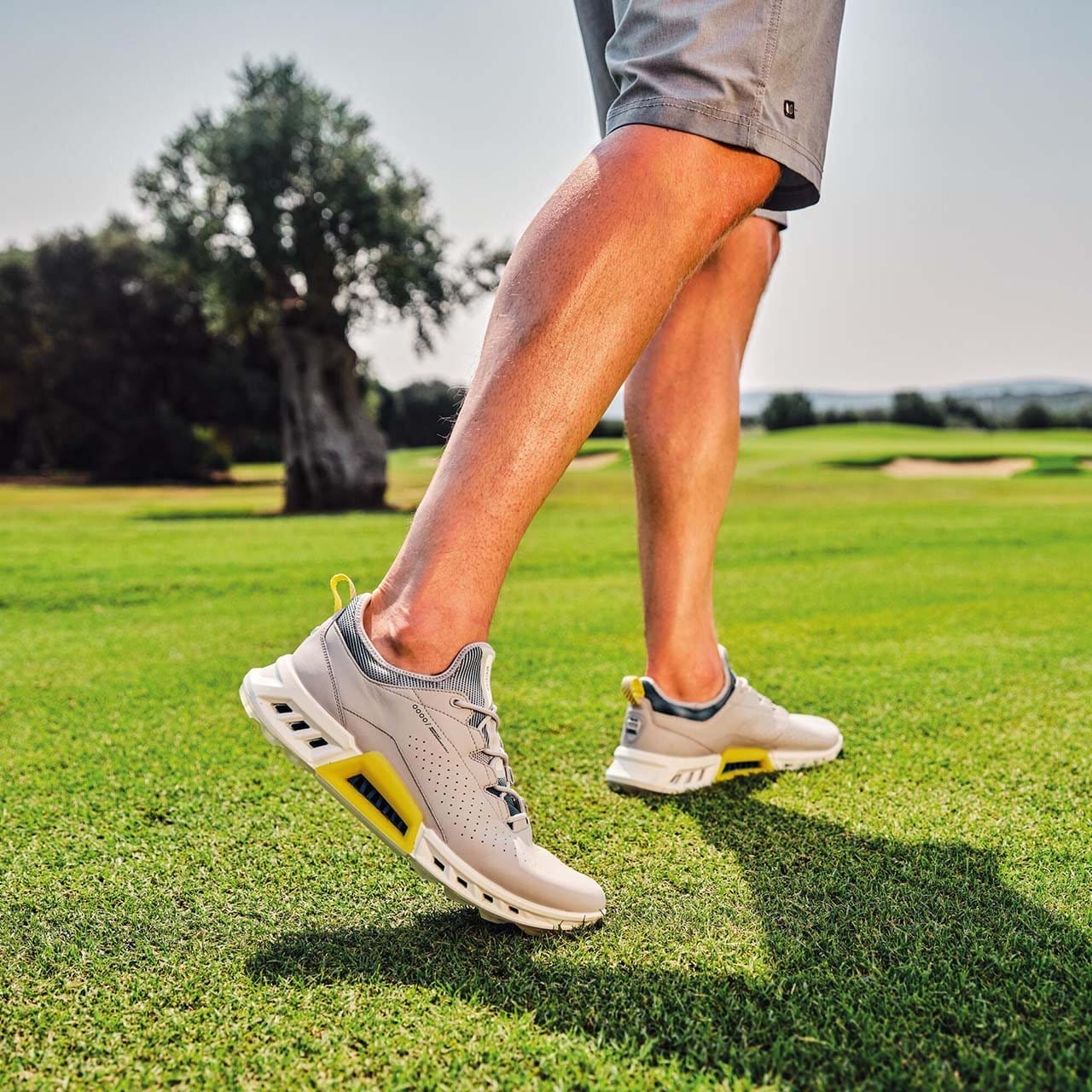 Man on golf course wearing gray and yellow golf shoes