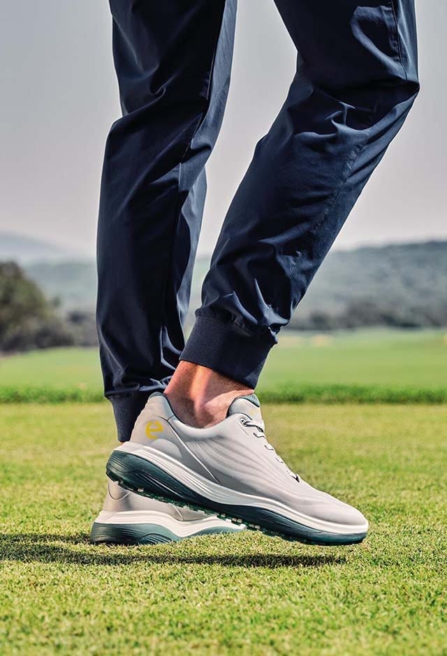Man on golf course wearing gray and green golf shoes